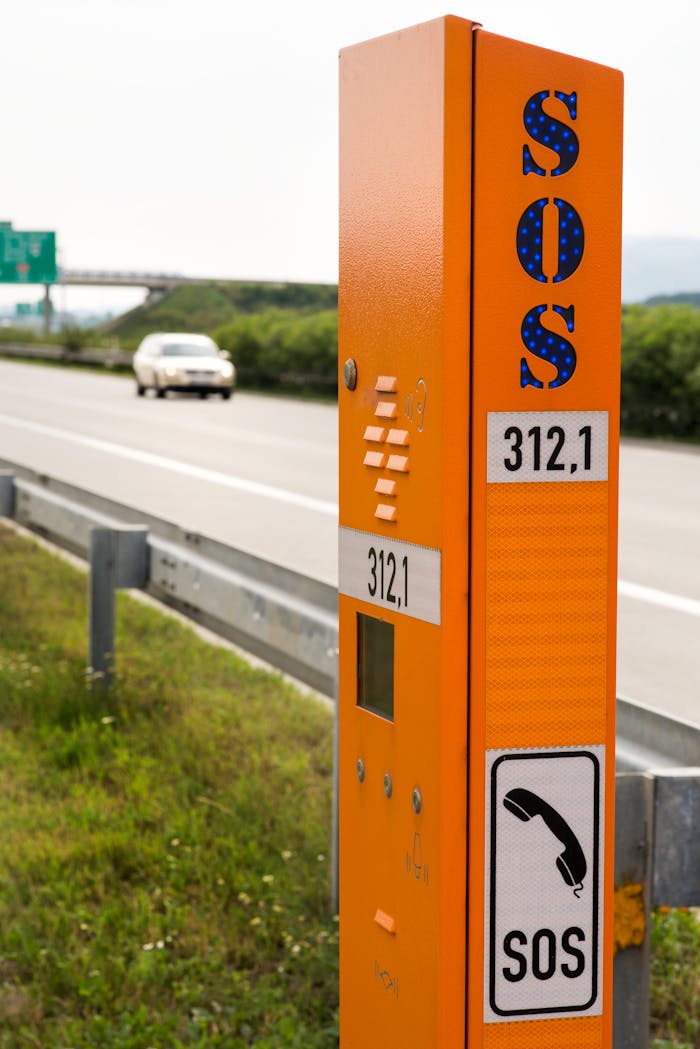Orange SOS emergency phone on a highway with a blurred car in the background.