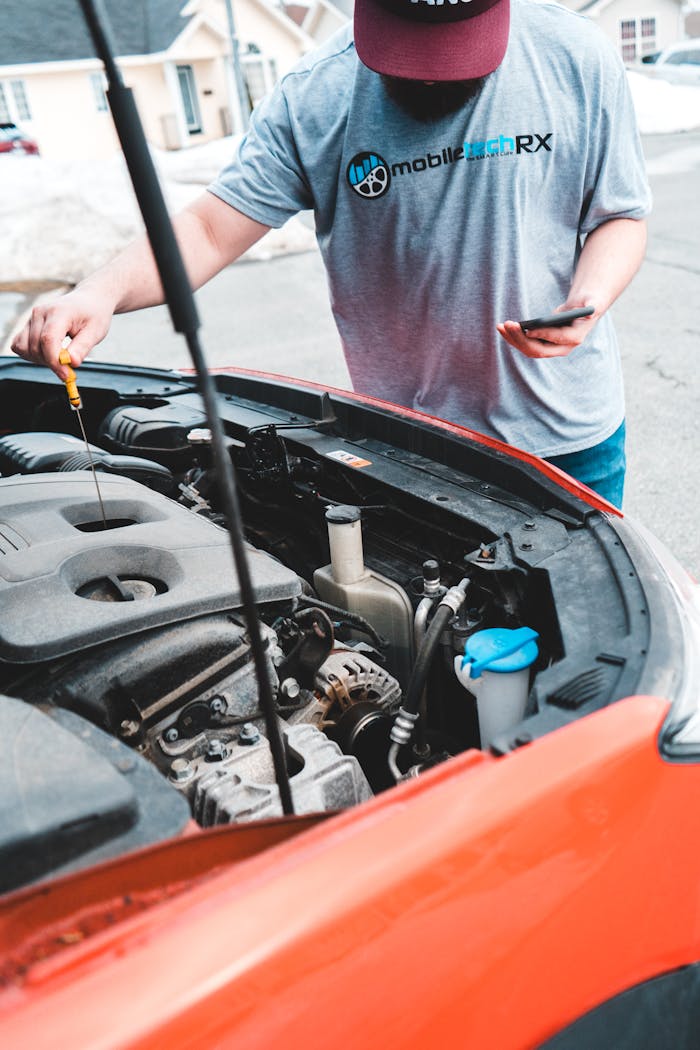Man inspecting car engine while holding phone outdoors, checking oil levels.