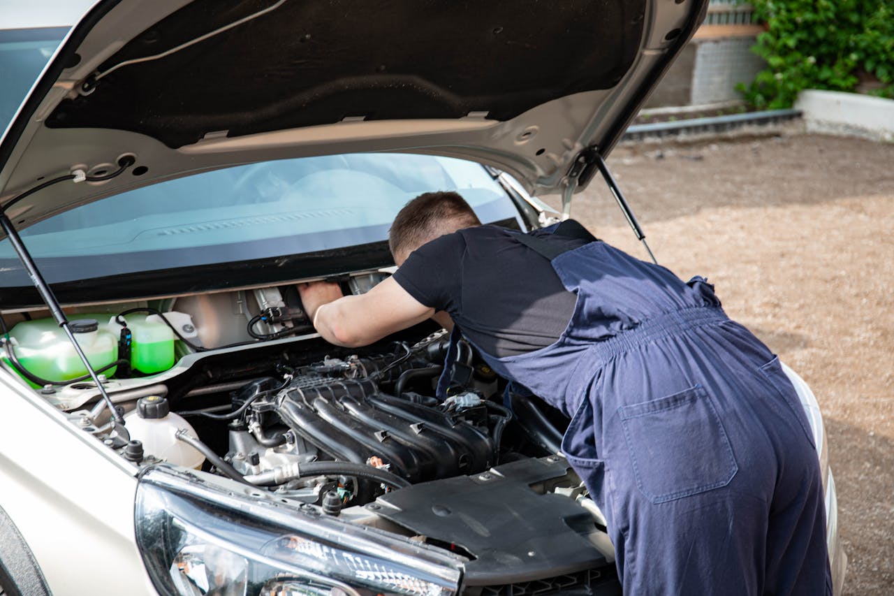 Mechanic repairing car engine in daylight, showcasing technical skills.